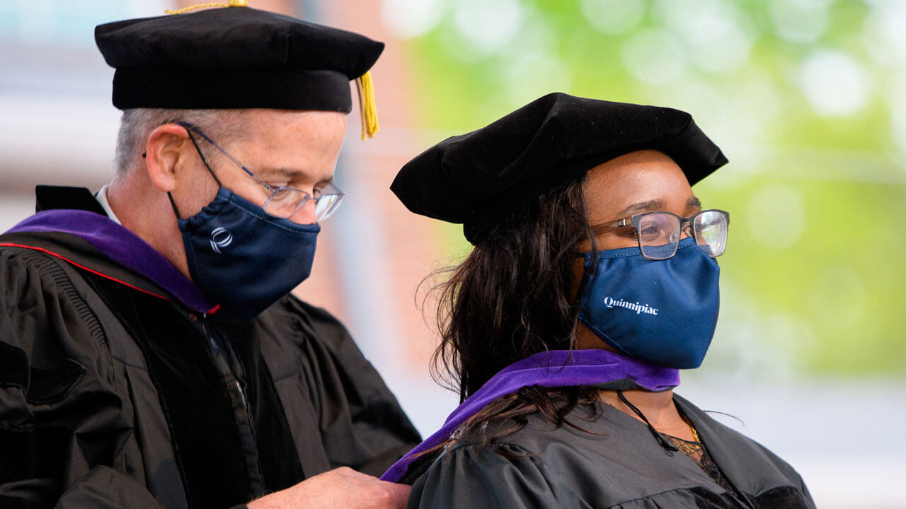 A faculty member adjusts a graduate's doctoral hood