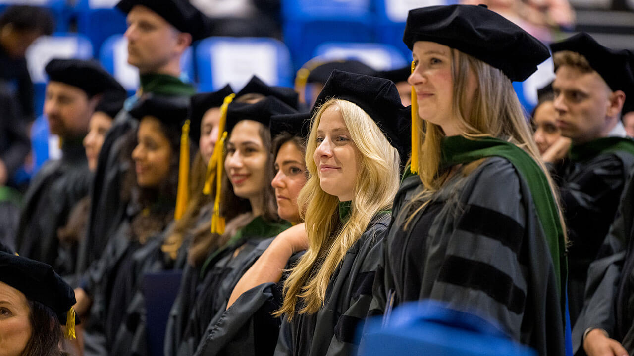 row of female graduates smile in their caps and gowns