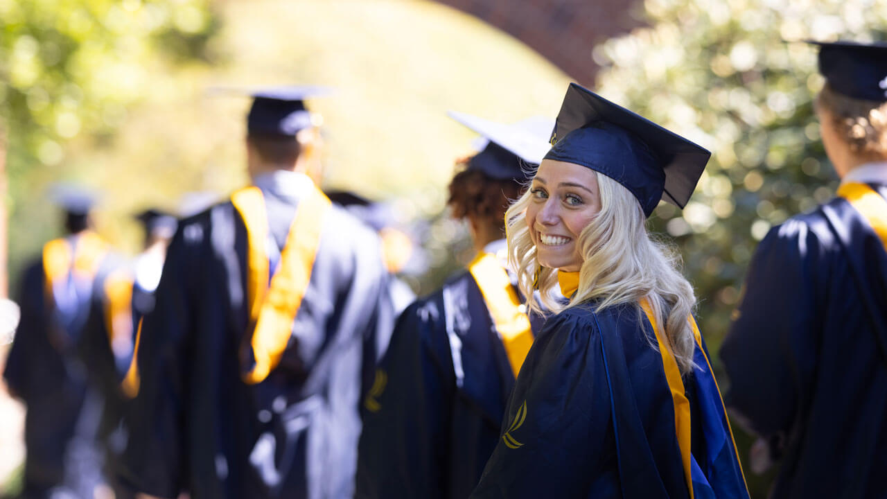 In cap and gown, a student of the graduating class of 2024 from the School of Business smiles proudly in celebration.