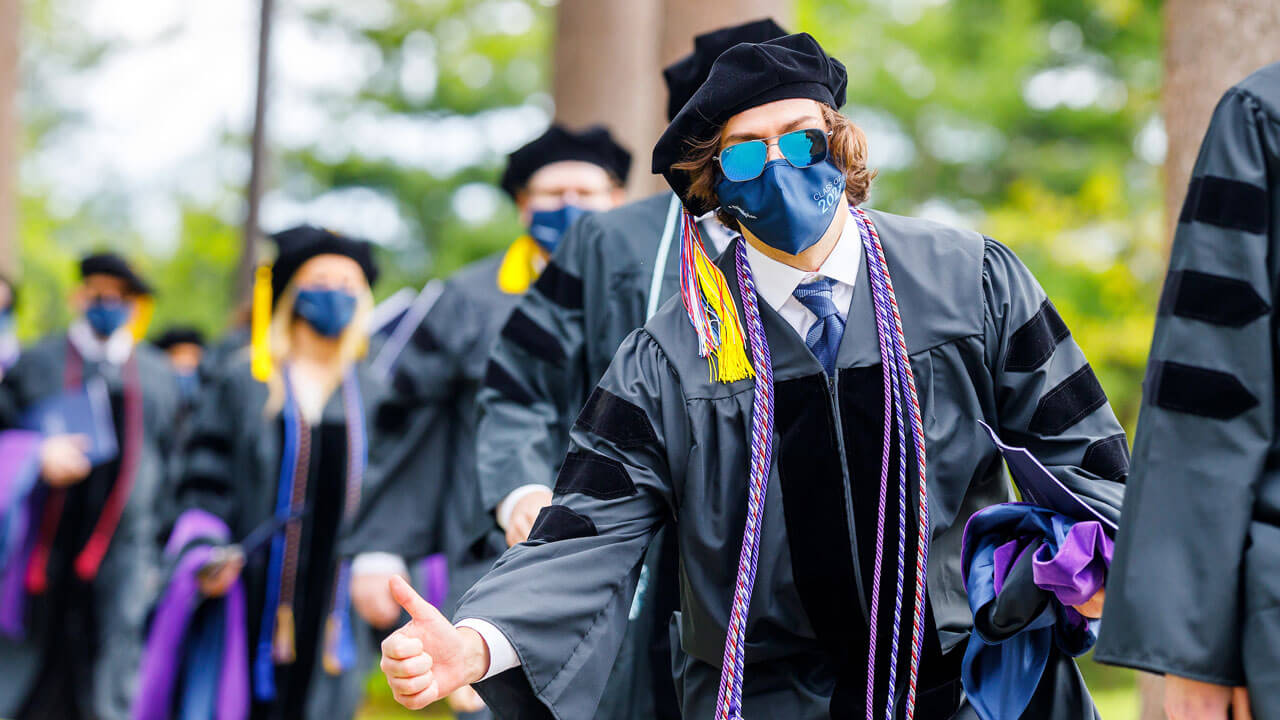 A graduate wearing reflective sunglasses gives a thumbs up