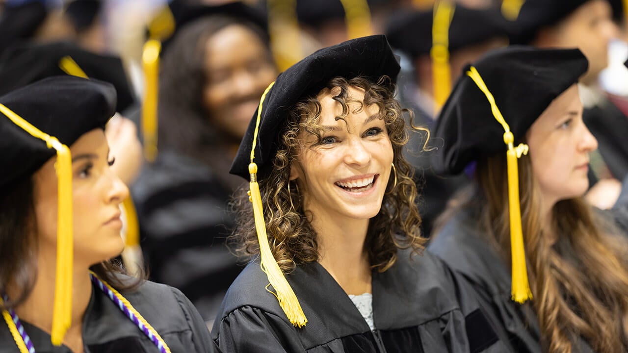 Graduate seated in line smiles to a friend