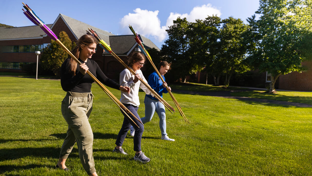 Students walk outside with hand-made spears in their anthropology course.