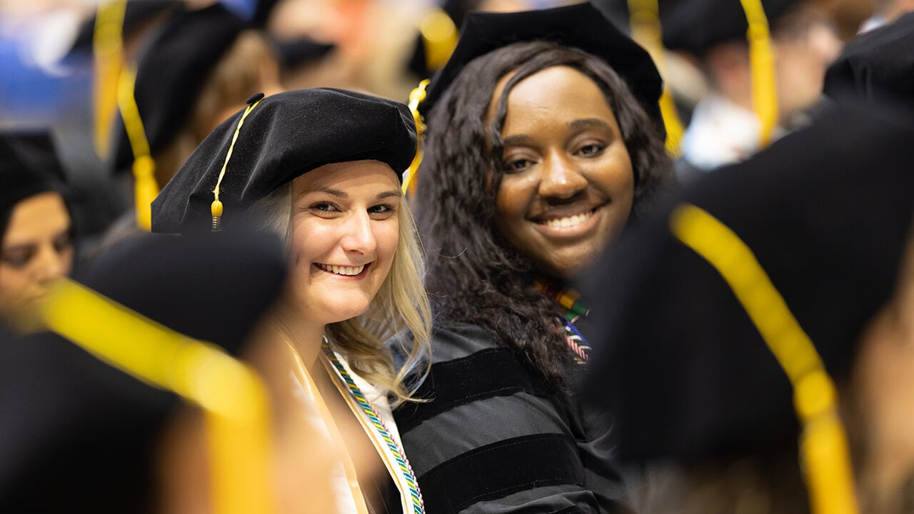 Graduates smile together while seated during ceremony