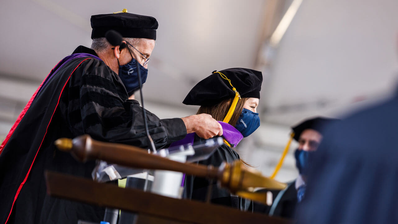 A professor drapes a doctoral hood on a graduate