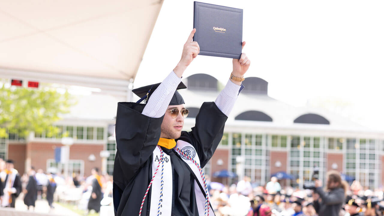 Student holds diploma showing the audience on stage