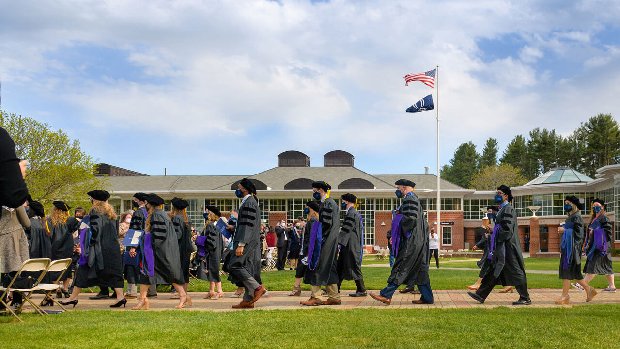 Graduates walk down the quad path under a blue sky