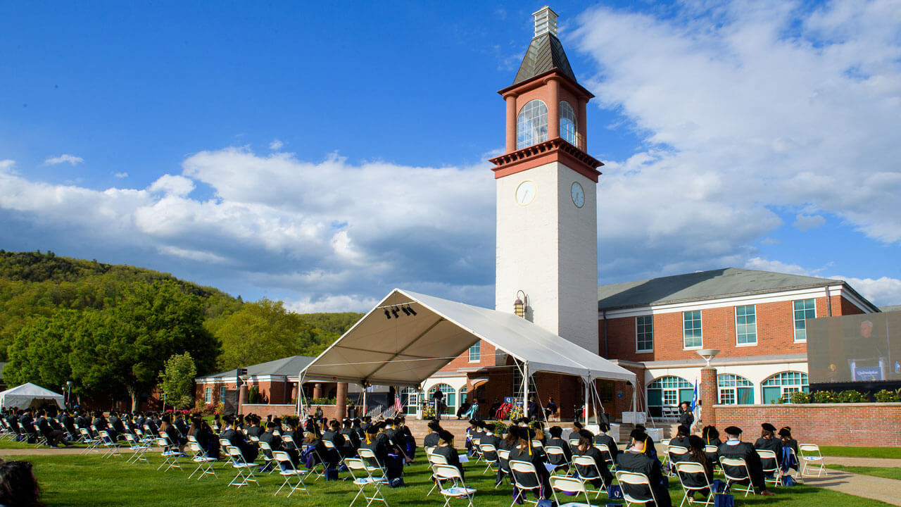 The sun shines on the library clocktower and the guests seated at Commencement