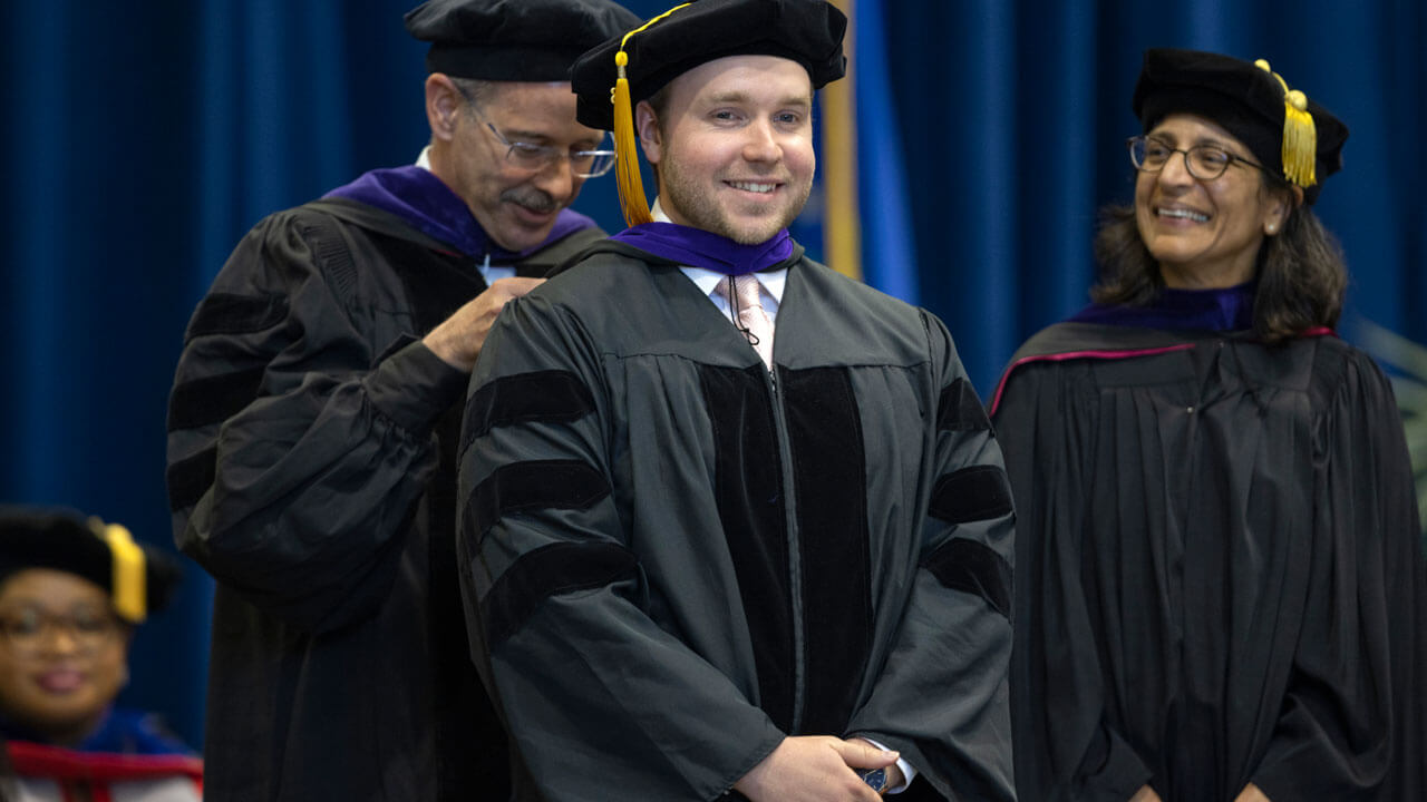 Student smiling to receive hood during graduation ceremony