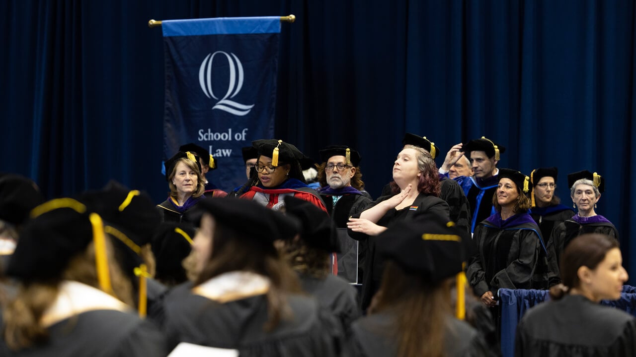 Professors and administrators stand on stage in front of dozens of law graduates
