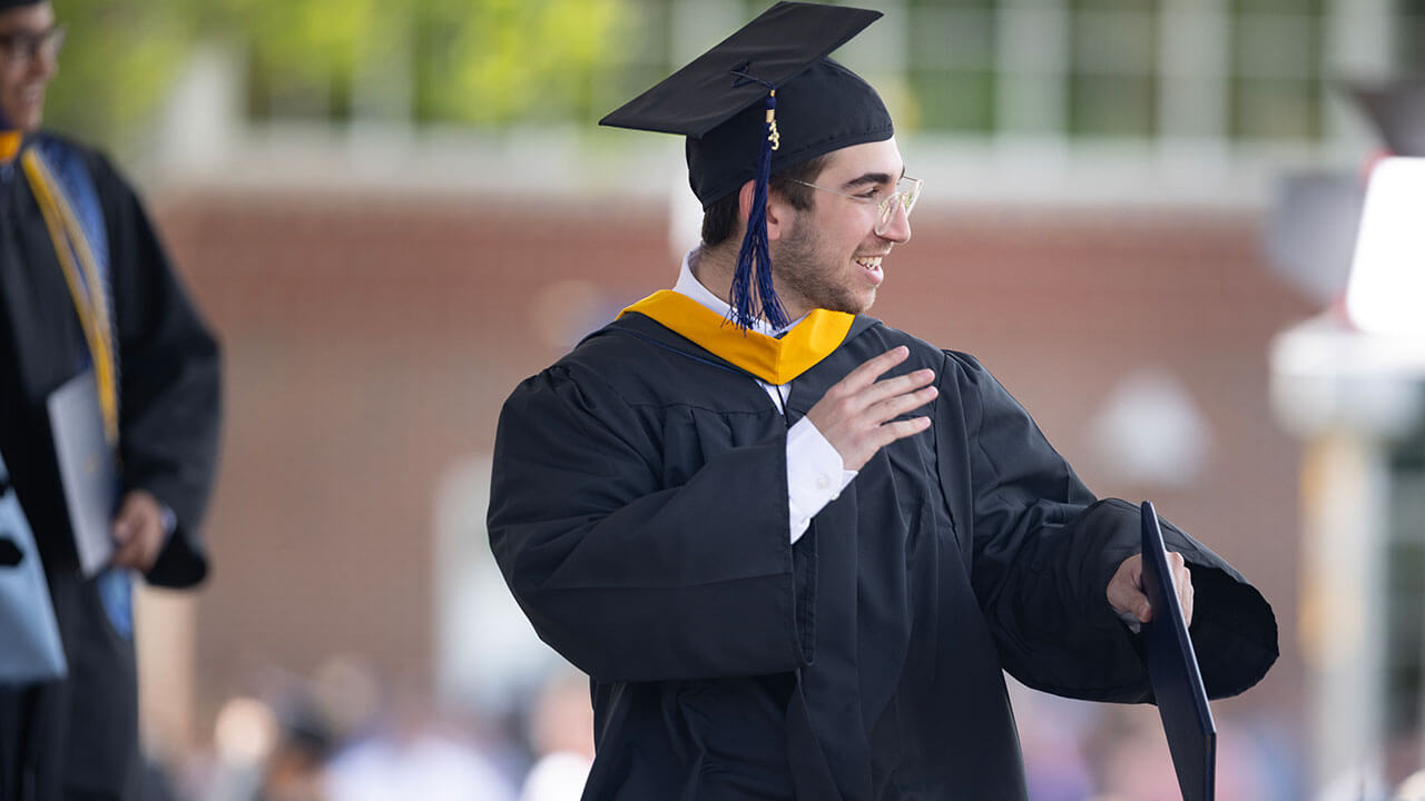 Student in cap and gown waving to the crowd