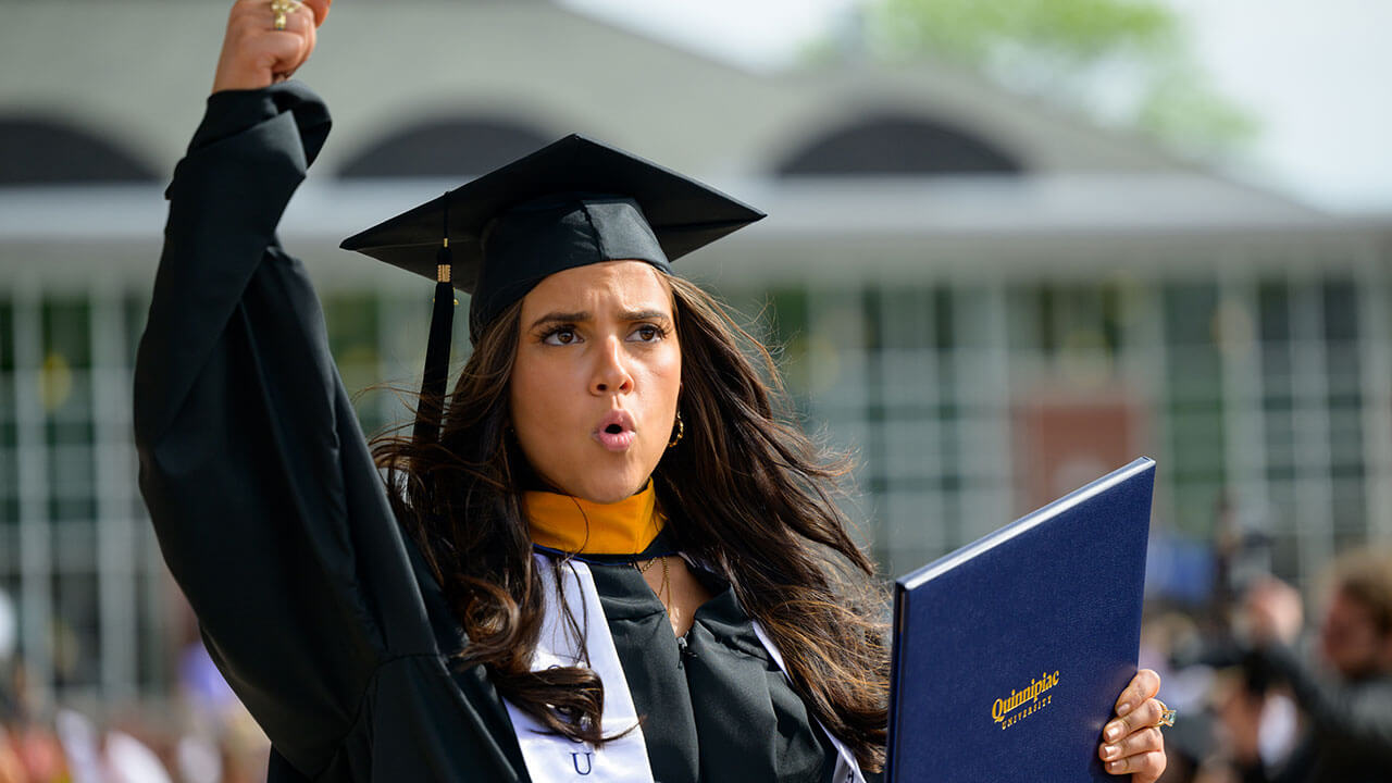female graduate fist bumps the air after receiving her diploma