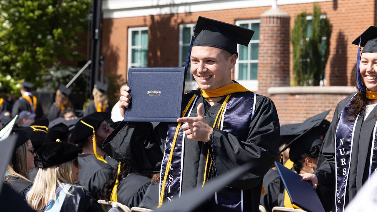 graduate makes a pointing gesture at the audience with his diploma