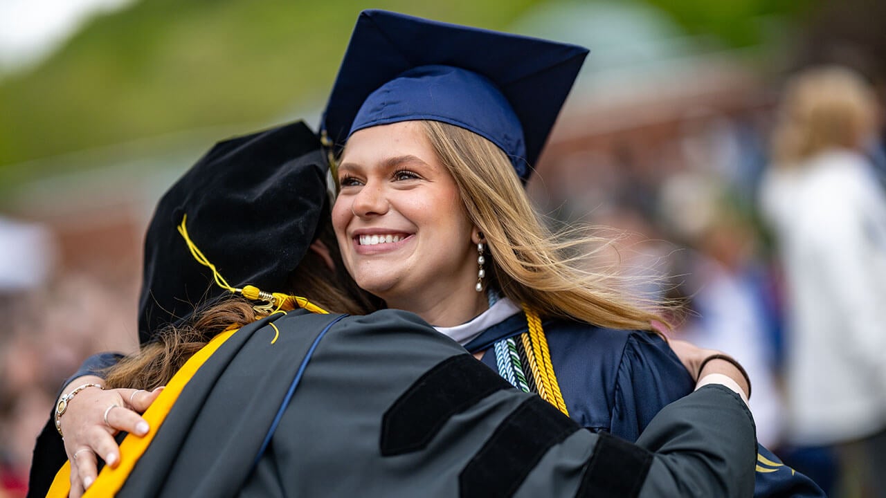graduate hugs professor smiling