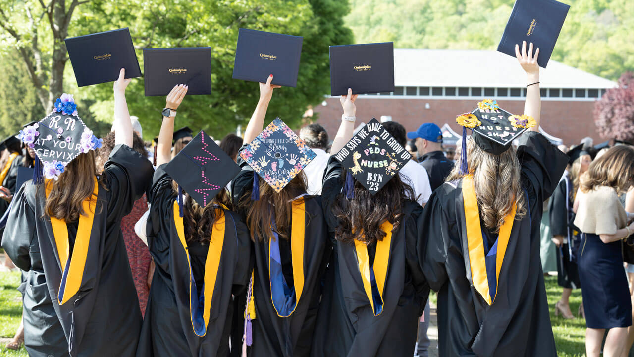 Graduates facing backward wearing decorated caps and holding up their diplomas
