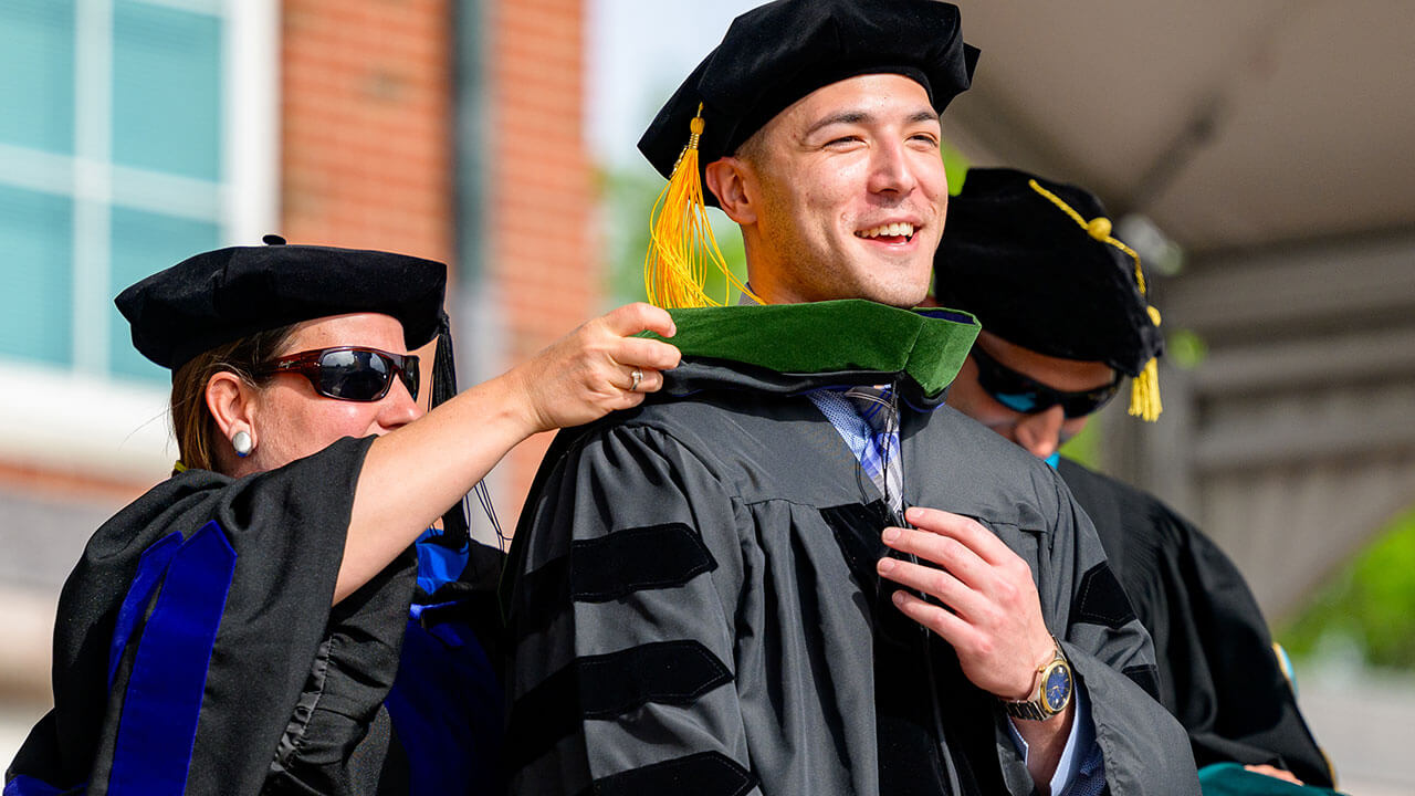 male graduate laughs happily as his hood is placed over him