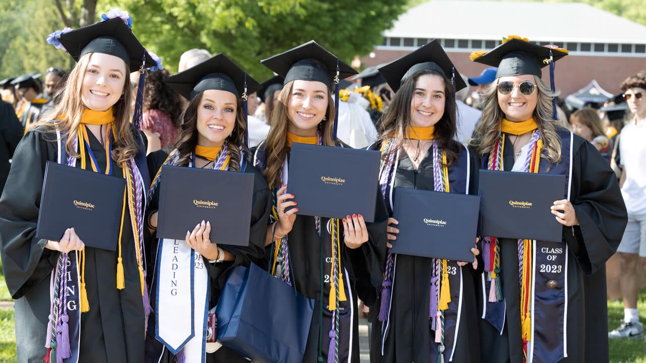 Five graduates pose for a photo with their diplomas