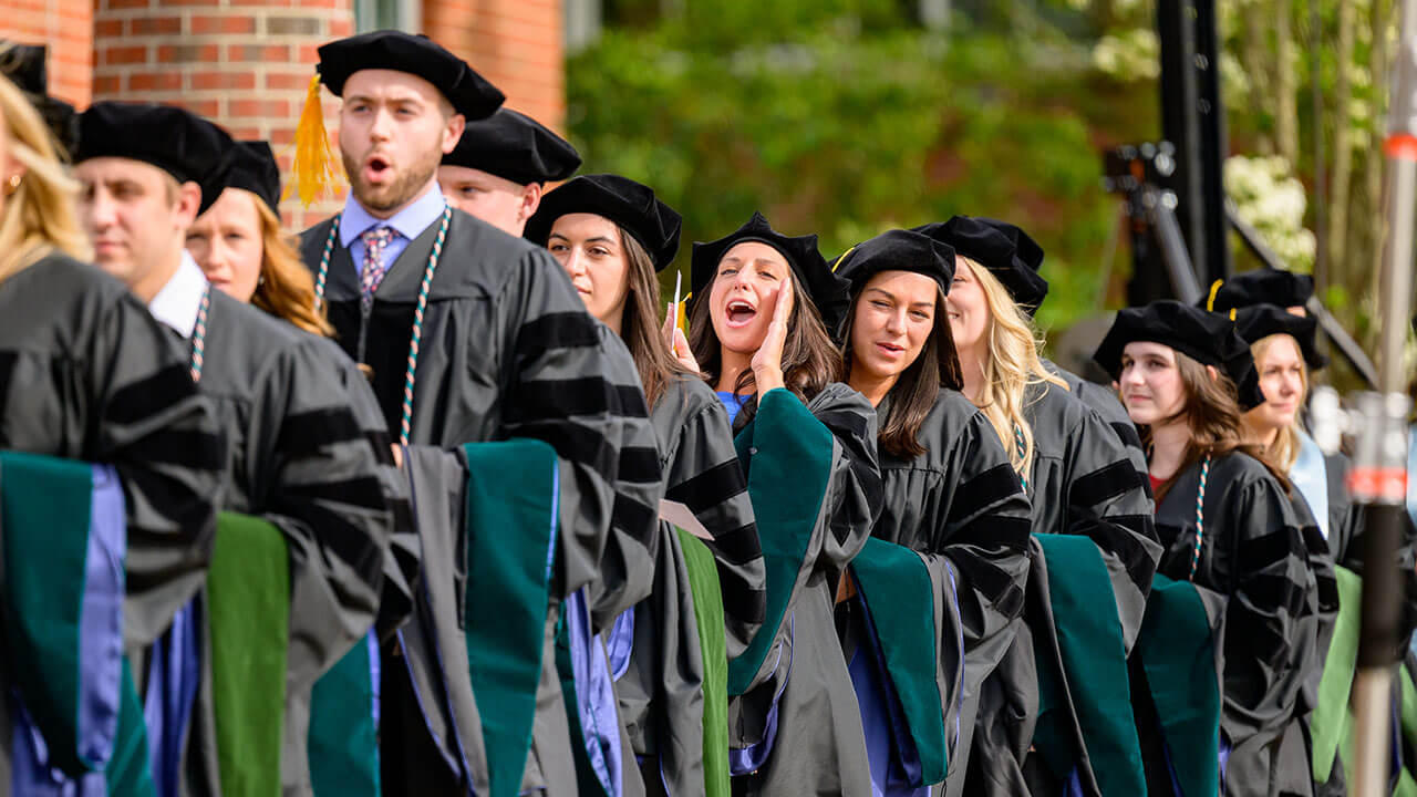 graduates smile and cheer from their line on the quad