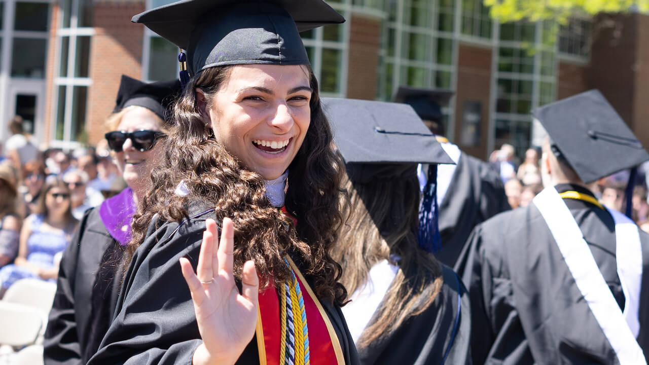 A graduate smiles and waves as she walks back to her chair
