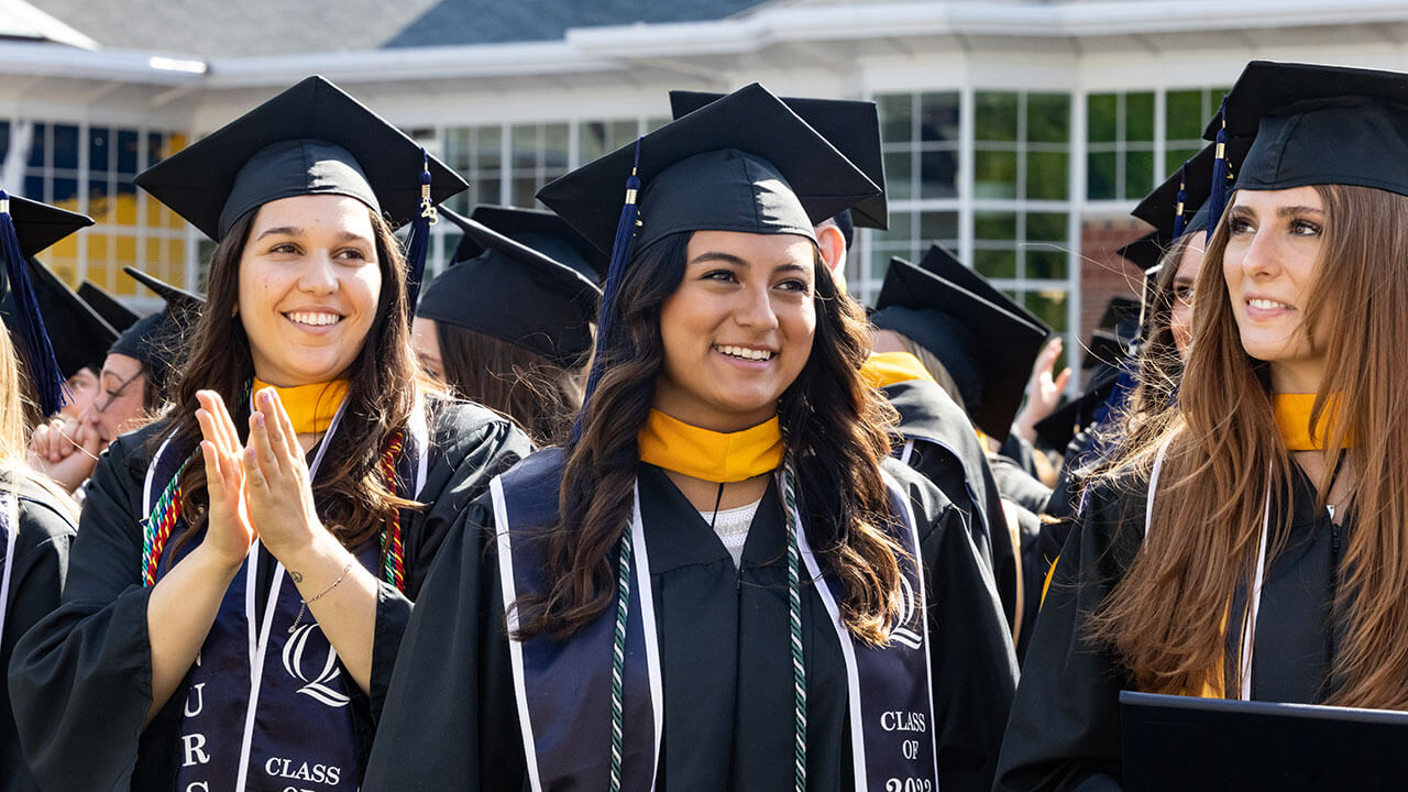 graduates smile and applaud while standing in their row