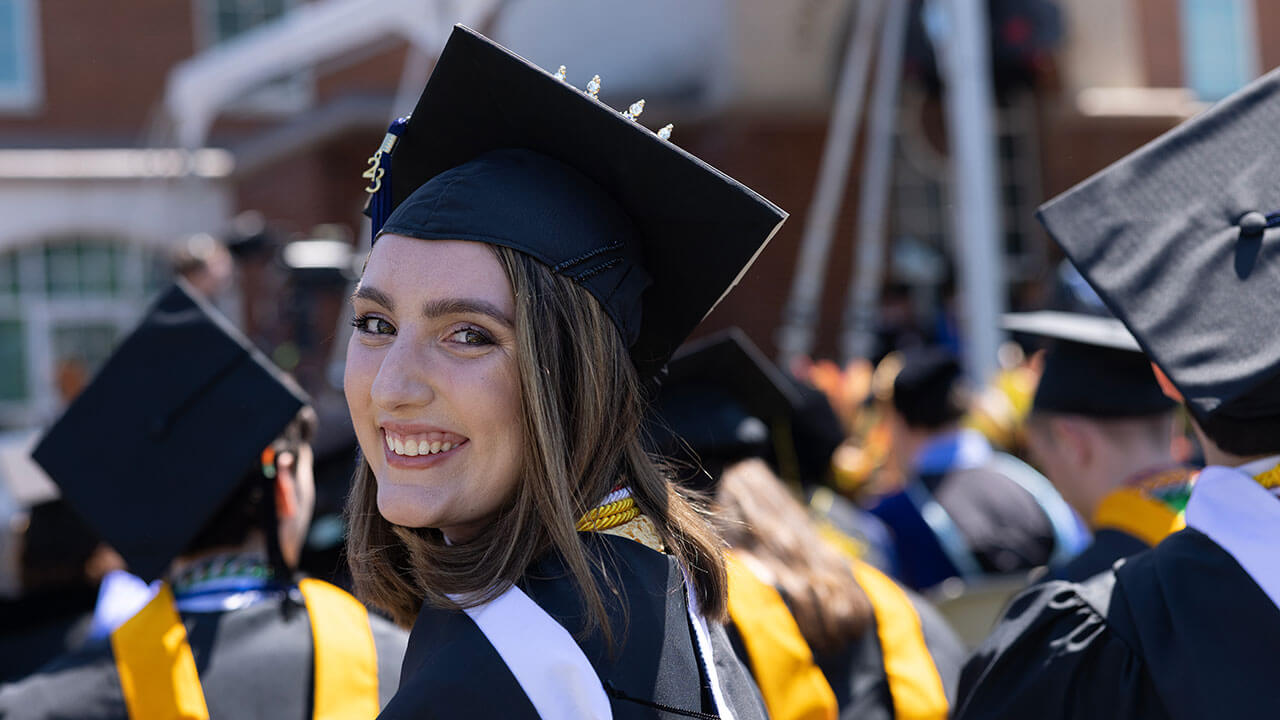 graduate turns and smiles at the camera over her shoulder