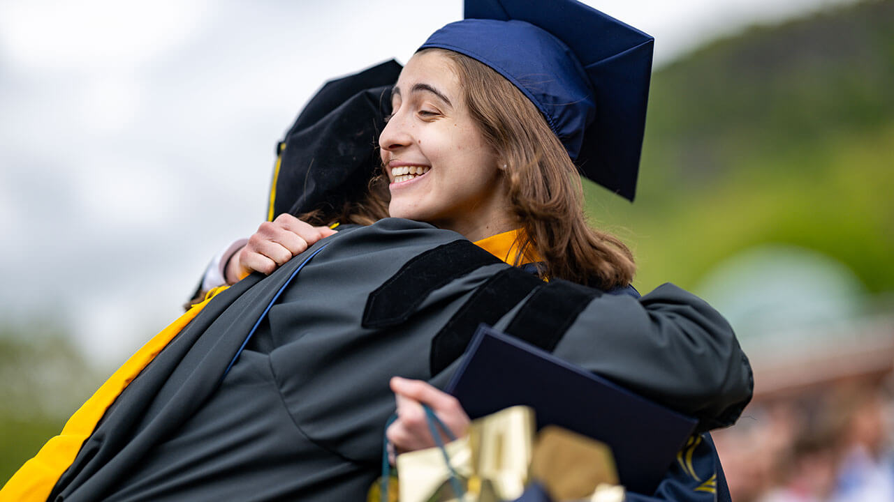 graduate hugs professor while smiling