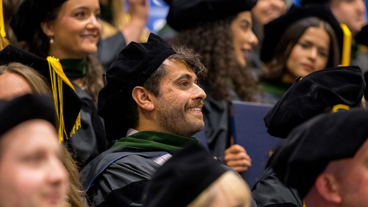 Dozens of graduates smile with their diplomas