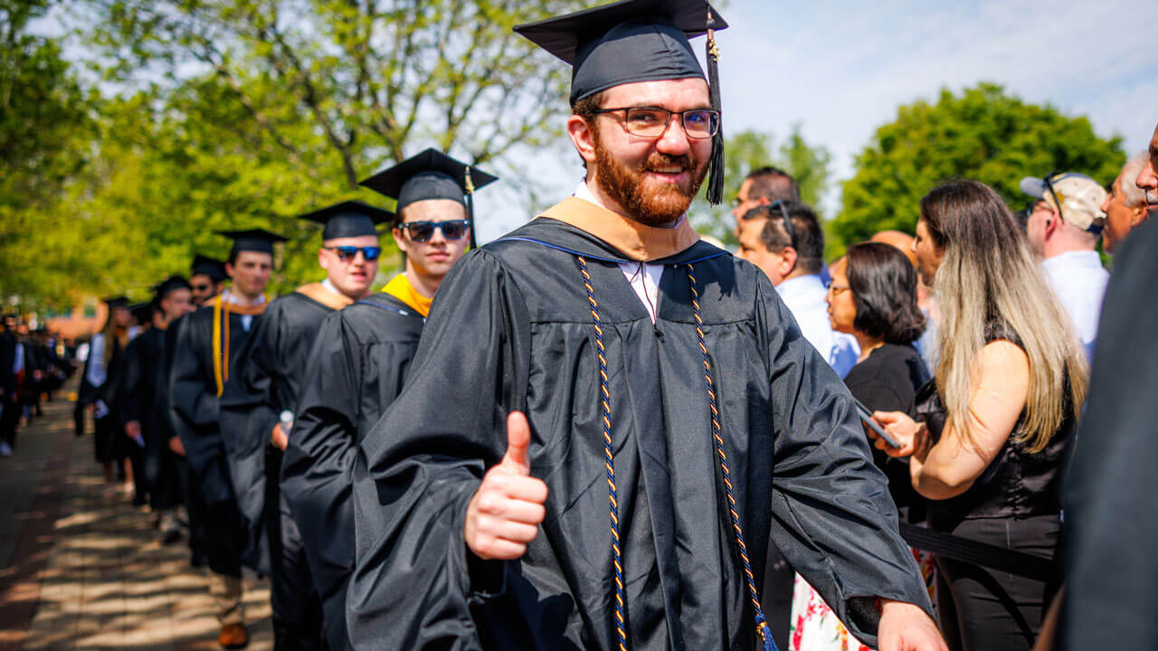 Graduate giving photographer thumbs up while walking to sit for commencement