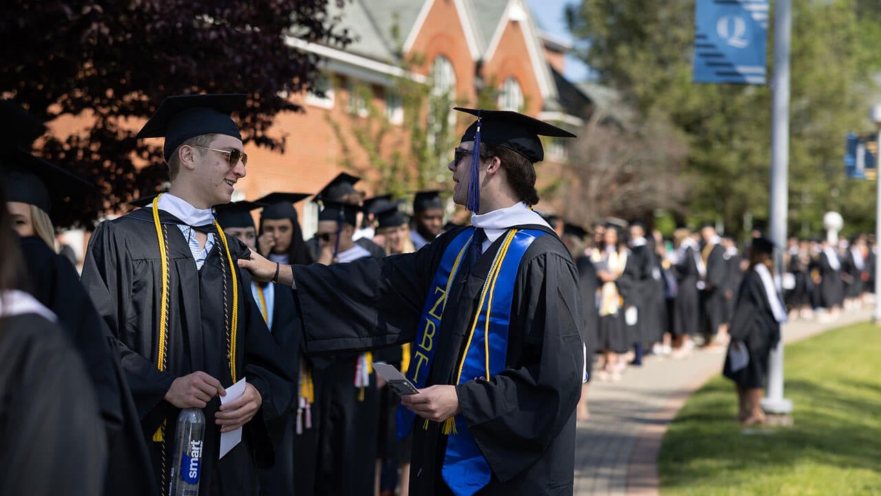 two male graduates reach out to each other in their processional line