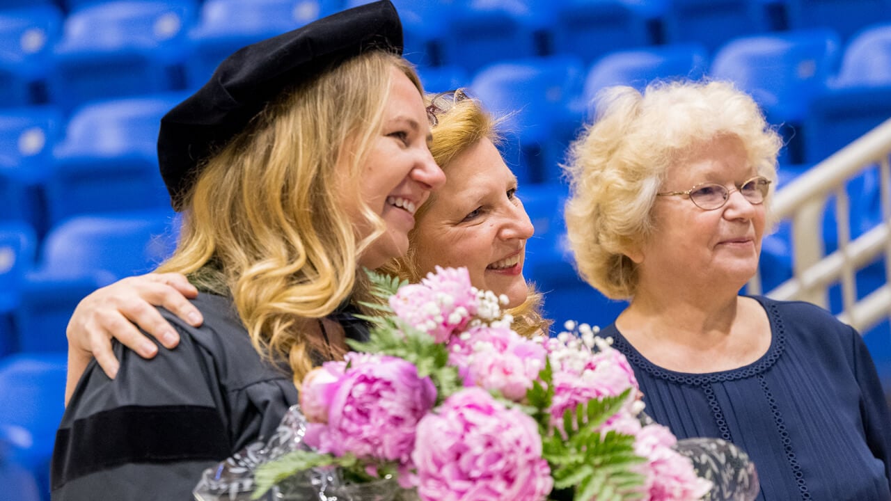 A graduate holds a bouquet of pink flowers and poses for a photo with her family