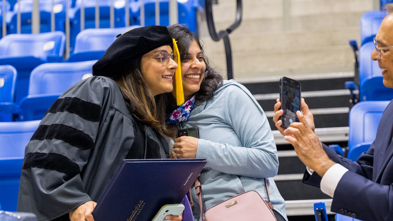 A graduate and family member pose for a photo in the arena