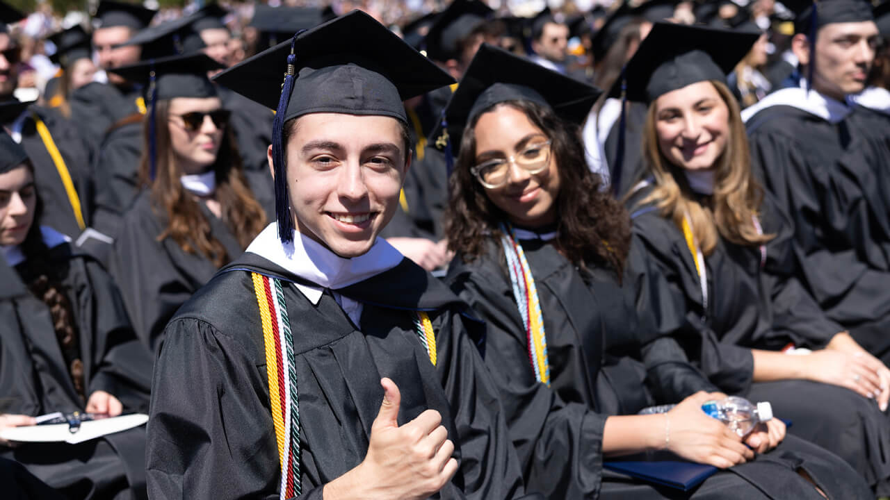 A graduate gives a thumbs up among dozens of other graduates