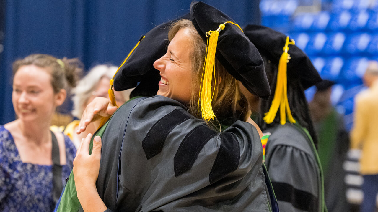 A graduate smiles broadly as she gets a hug from her friend