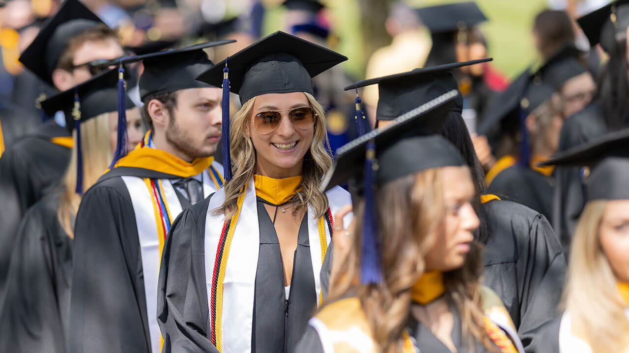 Business student smiling with sunglasses on in her cap and gown