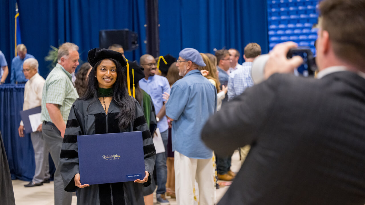 A graduate holds her diploma as she poses for a photo