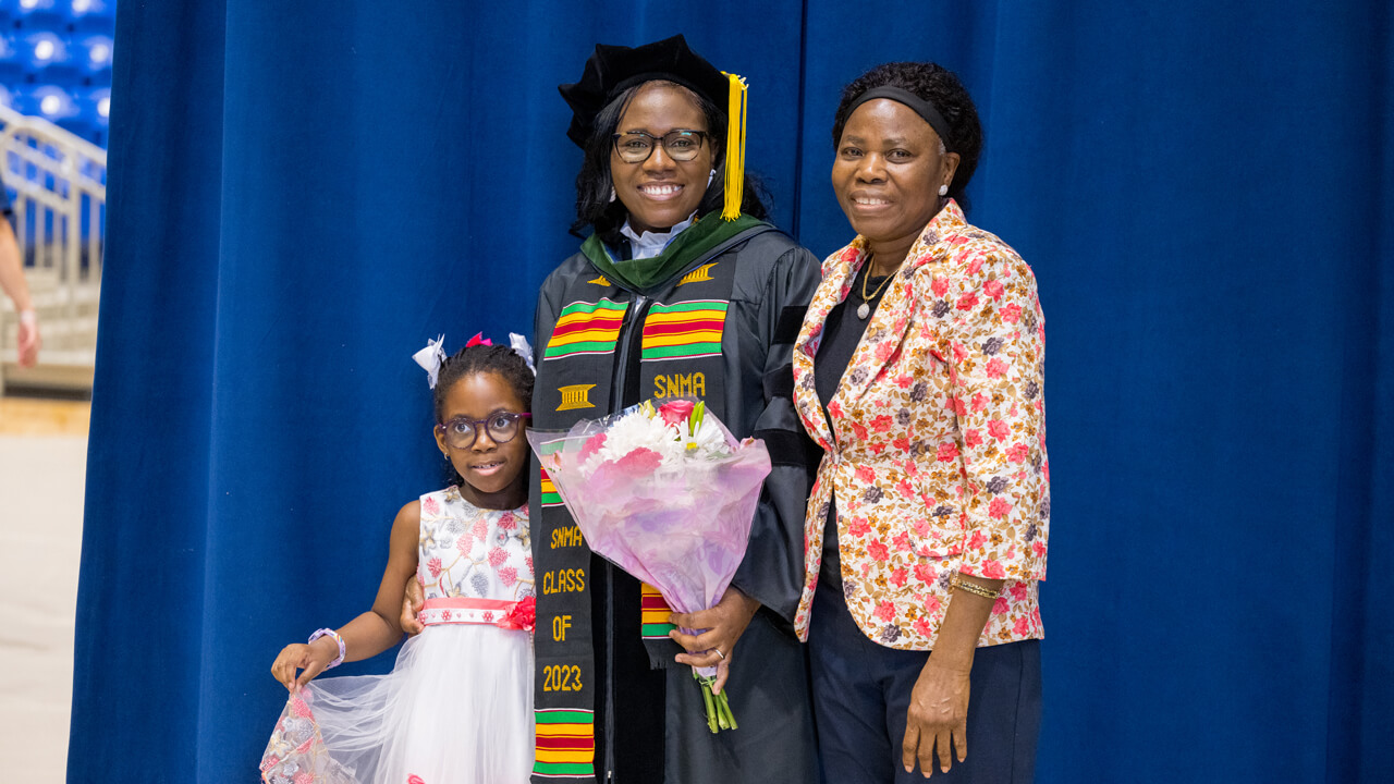 A graduate holds flowers and poses for a photo with family members