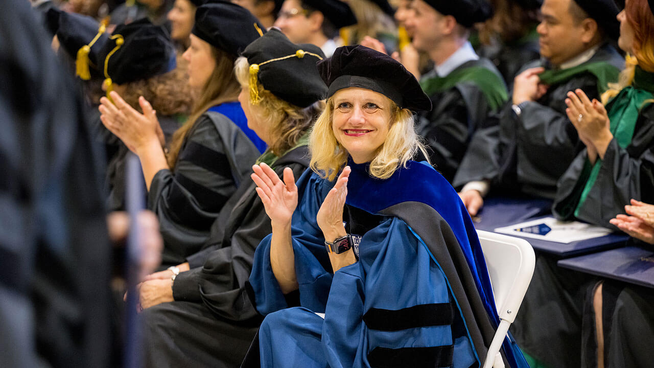 doctoral graduate in a blue robe claps and smiles at something near the camera