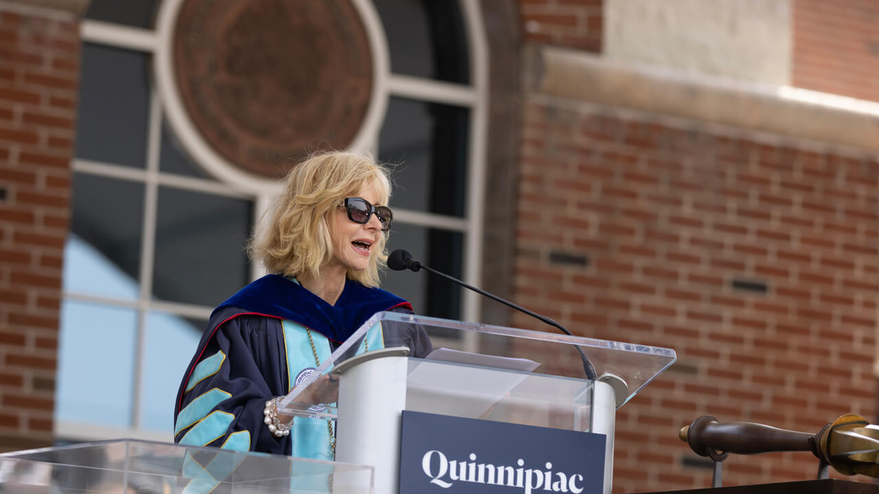 President Judy Olian wears commencement robes and speaks at a podium