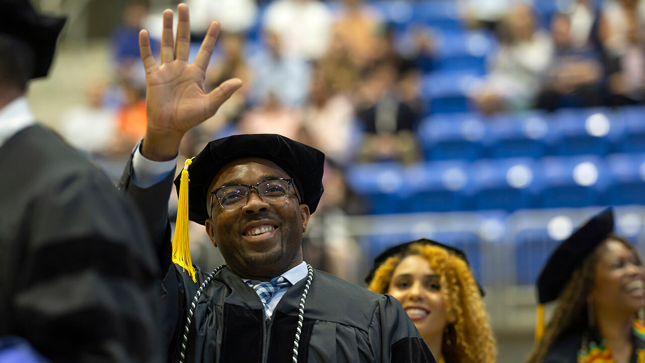 Graduate waves at crowd while smiling