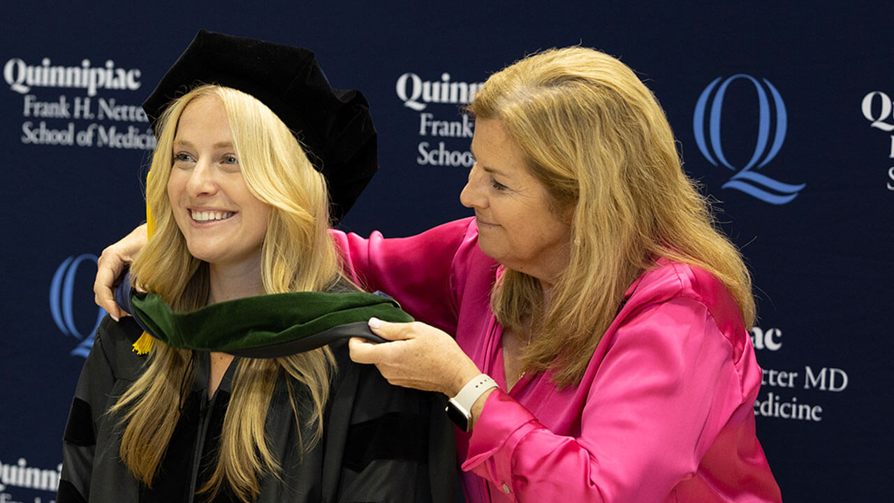 school of medicine graduate receives a green hood by a woman in a pink blazer