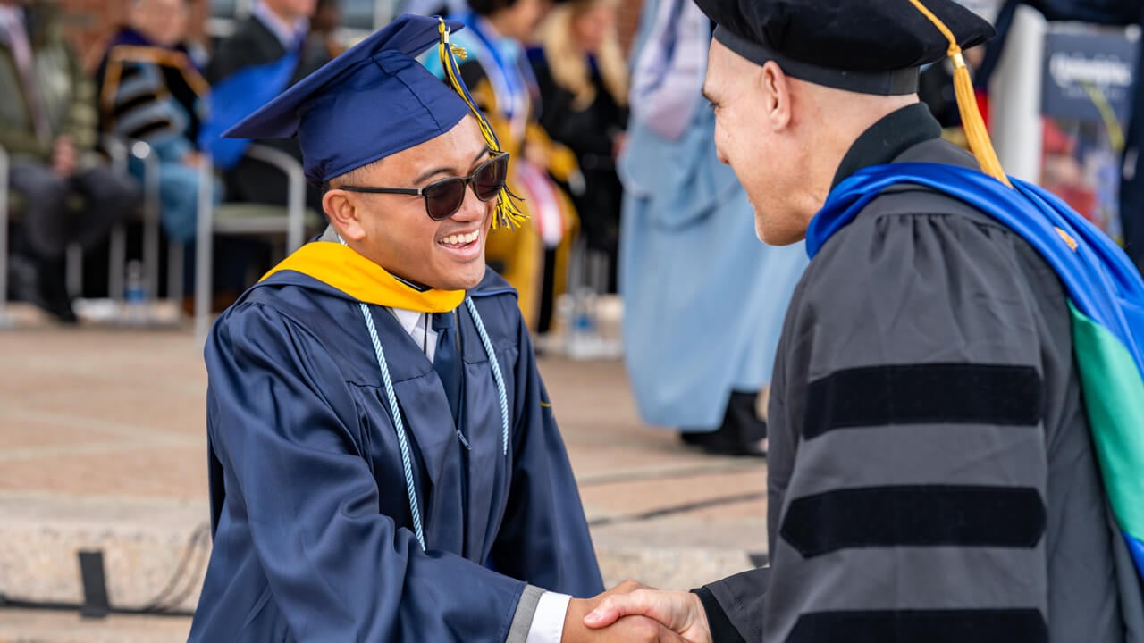 A graduate smiles as he shakes hands with Professor John Powers