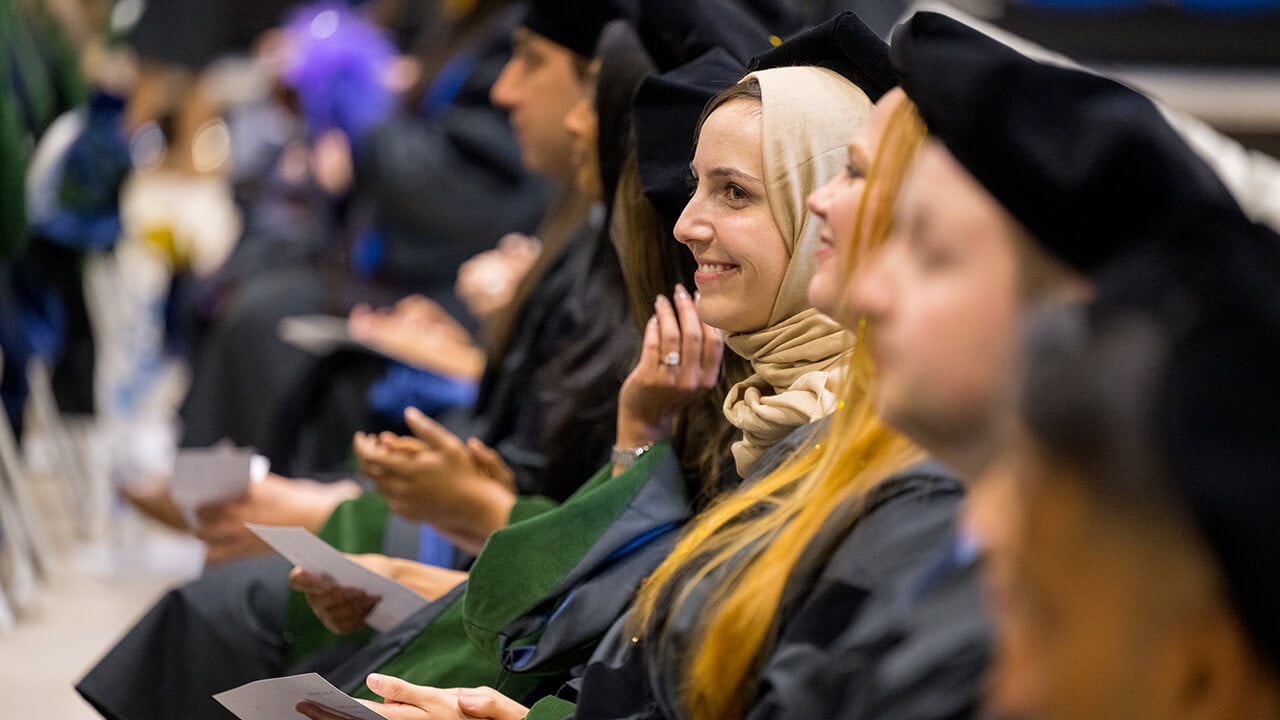 Graduates sit in line in the crowd and smile