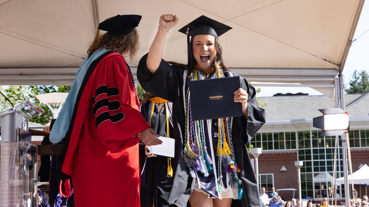 Graduate gestures to the air cheering loudly while holding her diploma