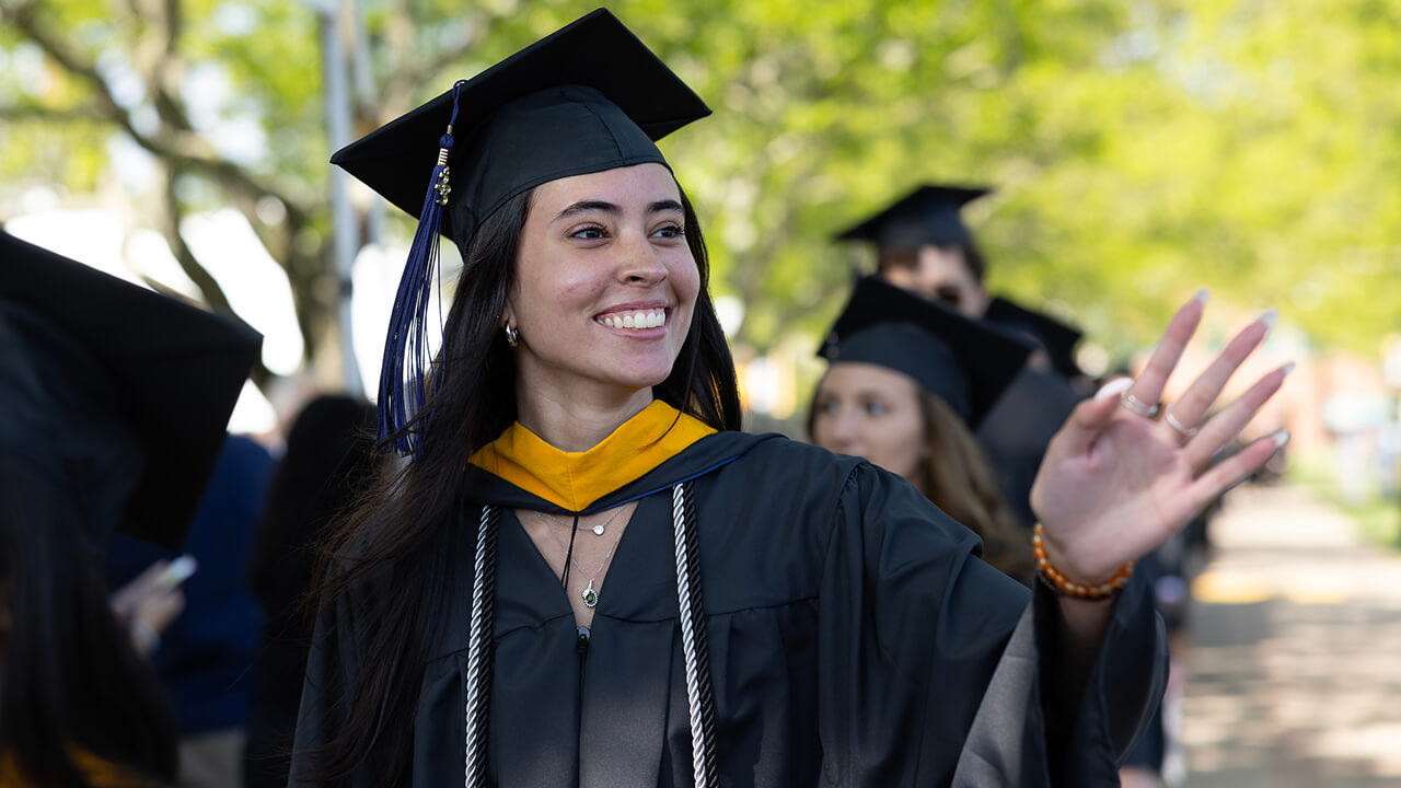 Graduate smiles and waves at crowd while processing in