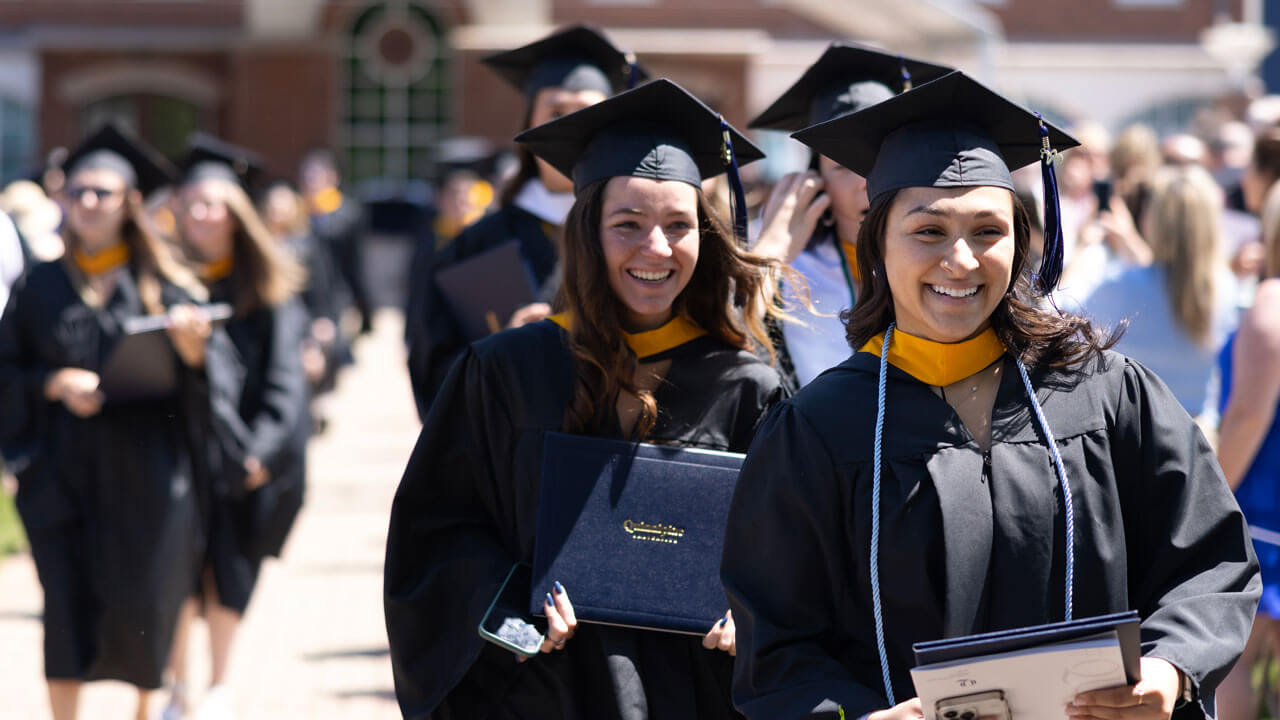 Two graduates holding diploma and walking in a line