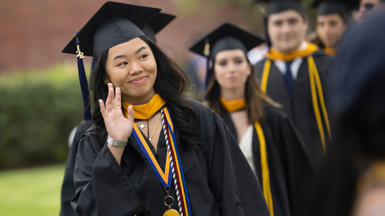 Graduate waves at the audience while walking to her chair