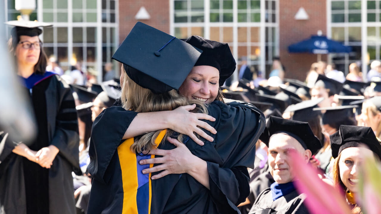 Two graduates big each other a big hug during the ceremony