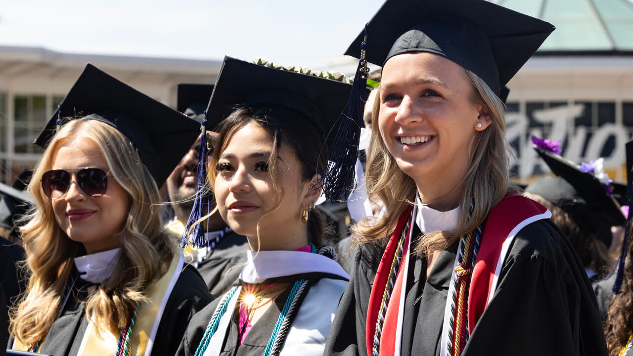 Graduates sit in a row and smile during the Commencement ceremony