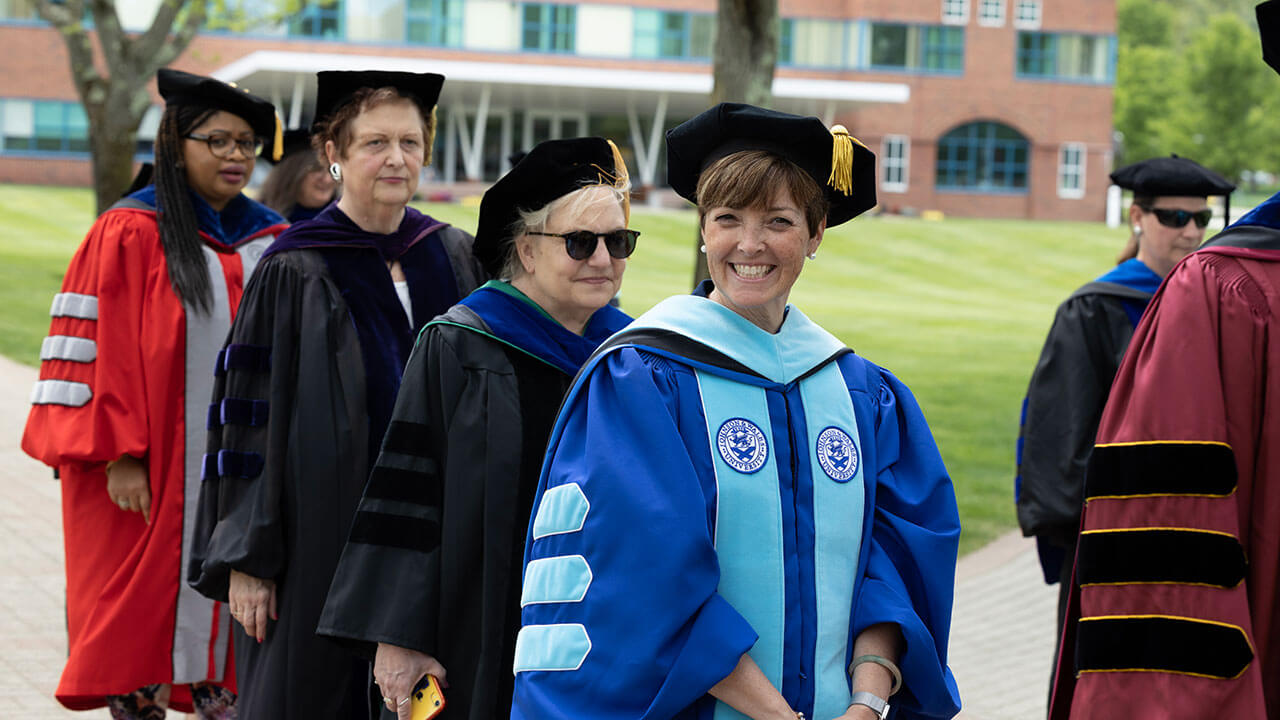 deans and other faculty line up for the procession, one looks at the camera and smiles broadly