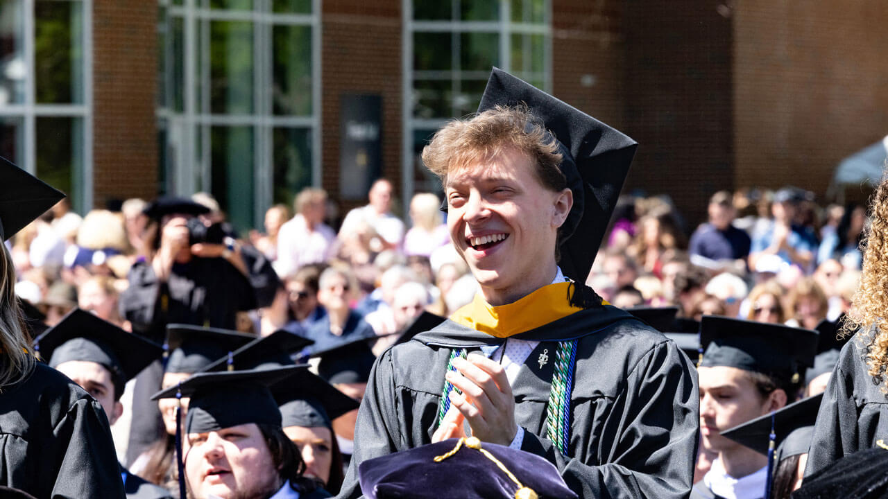 Graduate standing up and clapping during commencement