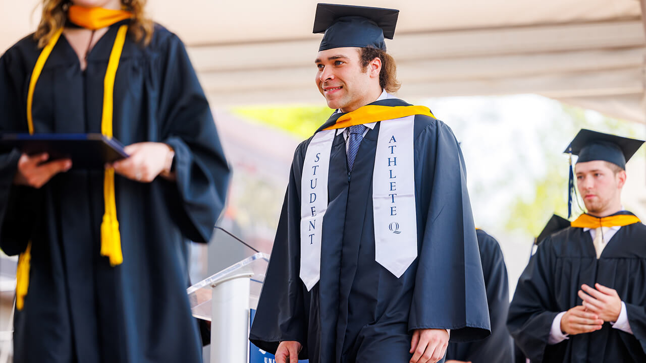 Graduate with student athlete stole walks on stage smiling